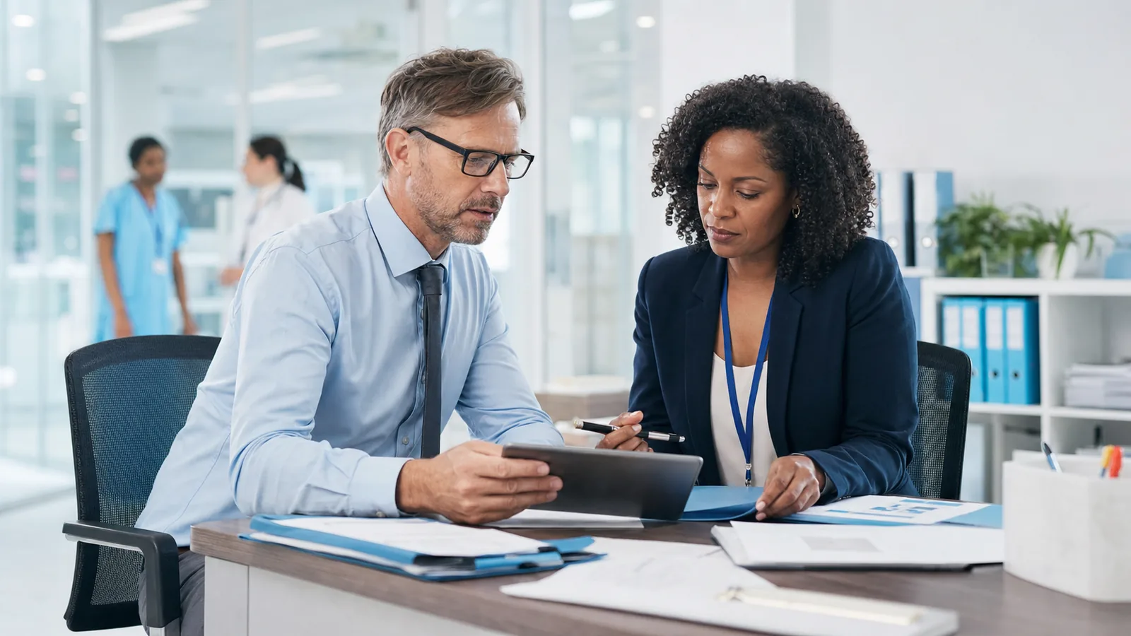 Healthcare administrator and technology consultant reviewing secure workflow planning in a clinical office.